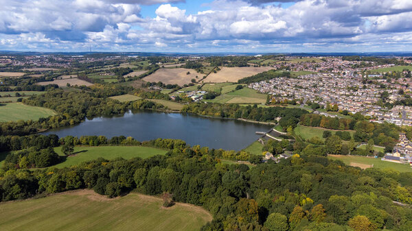 Aerial drone photo of the large Worsbrough reservoir in the village of Worsbrough, Barnsley in Sheffield in the UK, showing the British village and housing estates in the summer time