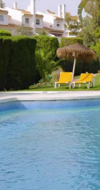 Yazın güzel bir yüzme havuzunun portresi. Arka planda sarı güneşlik ve palmiye ağaçları olan boş havuzu gösteriyor.