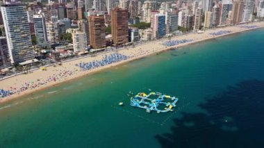 Güzel Benidorm şehrinin hava aracı görüntüleri okyanustaki devasa şişirilebilir saldırı kursunu, sahil önünü, otelleri ve apartmanları gösteriyor. Yaz mevsiminde güneşli bir gün.