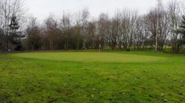 Kışın yeşil bir golf sahasının hava aracı görüntüleri soğuk bir kış gününde golf sahasında çıplak ağaçları gösteriyor.