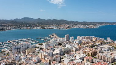 İspanya 'nın Balear Adaları' ndaki İbiza adasındaki Sant Antoni de Portmany kasabasındaki bir kumsalın insansız hava aracı fotoğrafı tekne limanını ve Playa de San Antonio olarak bilinen plajı gösteriyor.