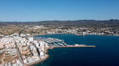 İspanya 'nın Balear Adaları' ndaki İbiza adasındaki Sant Antoni de Portmany kasabasındaki bir kumsalın insansız hava aracı fotoğrafı tekne limanını ve Playa de San Antonio olarak bilinen plajı gösteriyor.