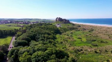 Aerial footage the famous Bamburgh Castle, a castle on the northeast coast of England, by the village of Bamburgh in Northumberland showing a drone view of the castle and sandy beach in the summer.