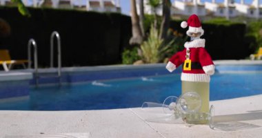 Güneşli bir günde iki şarap bardağıyla çevrili küçük bir Noel Baba kıyafeti giymiş bir şampanya şişesinin görüntüsü.