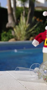 Güneşli bir günde iki şarap bardağıyla çevrili küçük bir Noel Baba kıyafeti giymiş bir şampanya şişesinin portre görüntülerini tarıyorum.
