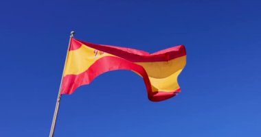 Güzel bir İspanyol bayrağının yavaş çekim görüntüleri. Güneşli bir yaz gününde gökyüzünde bulut olmadan rüzgarda dalgalanan İspanya bayrağını gösteriyor.