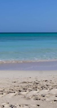Küba 'nın Varadero plajının önündeki güzel kumsalın portre görüntüleri güneşli bir yaz gününde gökyüzünde beyaz bulutlarla dalgaları ve temiz okyanus sularını gösteriyor.