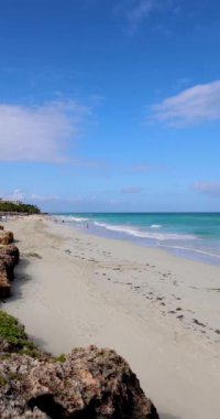 Küba 'nın Varadero plajının önündeki güzel sahilin portre görüntüleri güneşli bir yaz gününde kumsalda romantik bir yürüyüş yapan bir çiftle dalgaları ve temiz okyanus sularını gösteriyor.