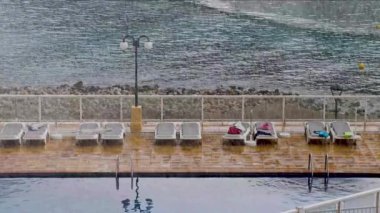 İspanya 'nın İbiza adasında yaz aylarında bir otelin yüzme havuzunun kenarındaki boş güneş pansiyonlarına yağan yağmuru gösteren bir tatil beldesinde şiddetli yağmur yağdı.