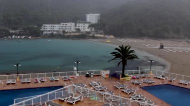 İspanya 'nın İbiza adasında yaz aylarında bir otelin yüzme havuzunun kenarındaki boş güneş pansiyonlarına yağan yağmuru gösteren bir tatil beldesinde şiddetli yağmur yağdı.