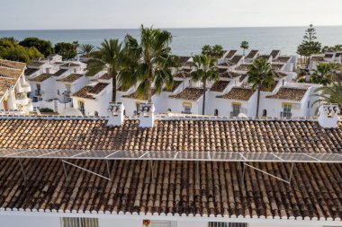 İspanya 'nın La Cala de Mijas kasabasındaki palmiye ağaçları ve okyanus ile çatıdaki güneş panellerinden gelen yenilenebilir enerjiyi gösteren tipik bir İspanyol apartman dairesi fotoğrafı.