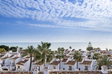 Tipik küçük bir İspanyol apartmanının, İspanyol evlerinin ve evlerinin fotoğrafları güneşli bir günde mavi okyanusu gören güzel sahil cephesine çıkıyor.