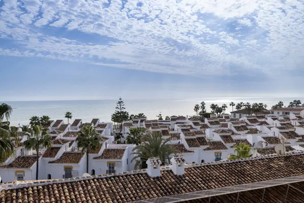 İspanya 'nın La Cala de Mijas kasabasındaki palmiye ağaçları ve okyanus ile çatıdaki güneş panellerinden gelen yenilenebilir enerjiyi gösteren tipik bir İspanyol apartman dairesi fotoğrafı.