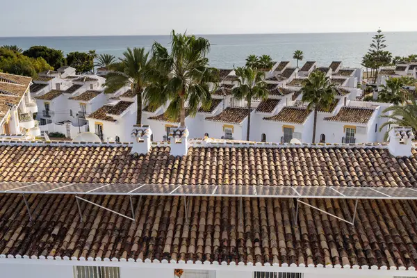 İspanya 'nın La Cala de Mijas kasabasındaki palmiye ağaçları ve okyanus ile çatıdaki güneş panellerinden gelen yenilenebilir enerjiyi gösteren tipik bir İspanyol apartman dairesi fotoğrafı.