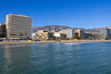 Malaga 'nın Fuengirola kıyı kasabasının önündeki güzel sahil fotoğrafında Aralık ayının güneşli bir gününde kumlu sahil, otel ve daireleri gösteren Costa Del Sol görülüyor.