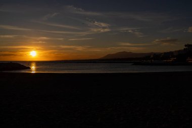 Kasabadaki sahil cephesinin ya da İspanya 'daki Marbella' nın akşam saatlerinde okyanusta batan güzel güneşi gösteren fotoğrafı.