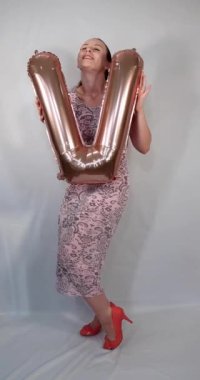 Uzun bir yaz elbisesi giymiş çekici bir kadının portre görüntüleri ve elinde aşk kelimesini heceleyen V harfi şeklinde altın bir balon tutan kırmızı tüyler.
