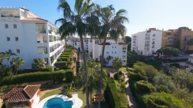 İspanya 'nın güzel Sitio de Calahonda kasabasının insansız hava aracı görüntüleri, İHA' nın güneşli bir günde büyük apartman kompleksleri boyunca iki palmiye ağacının arasında uçtuğunu gösteriyor.
