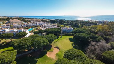 Aerial drone photo of a beautiful golf course in the town of Cabopino in Marbella Costa del Sol Spain with the ocean in the background and golfers on the first hole bunker of the golfing course clipart