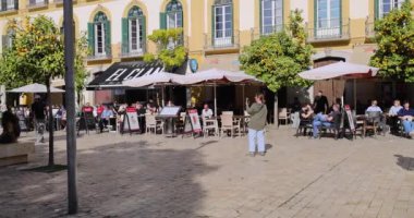 Malaga İspanya, 18 Ocak 2025: İspanya 'nın Malaga kentinin sokaklarının yavaş çekim görüntüleri, güneşli bir günde şehir meydanındaki restoranlarda insanların öğle yemeği ve içki içtiğini gösteriyor