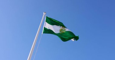 İspanya 'daki Endülüs bayrağının güneşli bir yaz gününde rüzgarda dalgalanan bir direkte bayrağı gösteren görüntüsü.