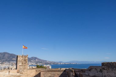 İspanya bayrağının açık güneşli bir yaz gününde Malaga 'nın Fuengirola kasabasında bulutsuz bir havada rüzgarda dalgalandığını gösteren fotoğraf.