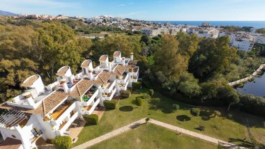 İspanya 'nın Malaga kentindeki güzel Sitio de Calahonda kasabasının hava aracı fotoğrafı güneşli bir günde ağaçlarla çevrili konut ve tatil evlerinin balkonlarını gösteriyor.