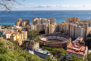 İspanya 'nın Malaga şehrinin sokaklarının fotoğrafı güneşli bir günde arka planda okyanus bulunan yüksek katlı apartman bloklarıyla çevrili ünlü tarihi boğa güreş ringini gösteriyor.
