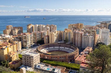 İspanya 'nın Malaga şehrinin sokaklarının fotoğrafı güneşli bir günde arka planda okyanus bulunan birçok apartman bloğuyla çevrili ünlü tarihi boğa güreş ringini gösteriyor.