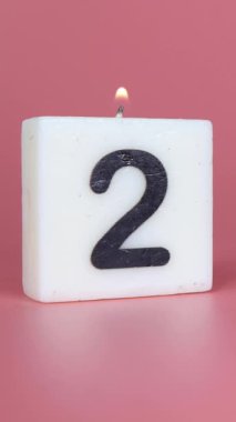 Dikey bir portre, kare bir mum. 2 numaranın bir doğum gününü veya yıldönümünü kutlayan pembe bir arka planda yanıp söndüğünü söylüyor.
