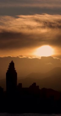 İspanya 'nın eski Benidorm kasabasında akşam vakti güneşin batışının portre görüntüleri gökyüzünde bulutlarla birlikte yükselen apartmanlar boyunca uzanan güzel sarı güneşin batışını gösteriyor.