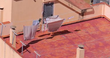 Bir İspanyol apartmanının tepesindeki çamaşır ipinde asılı kıyafetlerin yavaş çekim görüntüleri. Çamaşırların yüksek binanın tepesinde kuruduğunu ve rüzgarın temiz havada estiğini gösteriyor.