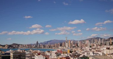 İspanya 'nın eski Benidorm kasabasına bakan görüntülerde Batı Sahili Gezinti Alanı yüksek katlı daireler ve binalarla çevrili, arkasında dağlar ve beyaz bulutlar var.