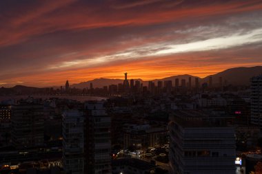 Benidorm İspanya, 20 Mart 2025: İspanya 'nın eski Benidorm kasabasında güneşin batışının fotoğrafı gökyüzünde bulutlarla birlikte gökyüzünde yükselen daireler boyunca uzanan güzel kırmızı güneşi gösteriyor