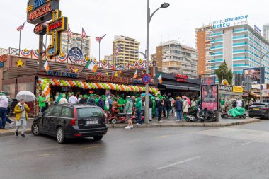 Benidorm İspanya, 17 Mart 2025: İspanya 'daki Benidorm kasabasının fotoğrafı, yağmurlu bir Mart ayında barların ve barların önünde Aziz Patrick Günü' nü kutlayan insanları gösteriyor.