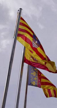 İspanya 'nın Alicante kentindeki Villajoyosa kasabasında güneşli bir günde İspanyol ve Valensiya toplumunun bayrağını gösteren sarı bir binaya 3 İspanyol bayraklı bir seçimin dikey görüntüsü.