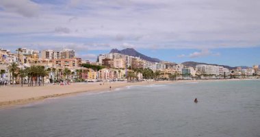 İspanya 'nın Villajoyosa kasabasındaki tipik bir İspanyol plajının yavaş çekim görüntüleri güneşli bir yaz gününde arka planda güzel sahil manzaralı otelleri ve dağları gösteriyor.