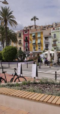 Villajoyosa, Valencia İspanya, 12 Mart 2025: Villajoyosa kasabasındaki tipik bir İspanyol sokağının dikey portresi palmiye ağaçları ve renkli restoranların bulunduğu caddeyi gösteriyor