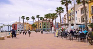 Villajoyosa, Valencia İspanya, 12 Mart 2025: İspanya 'nın Villajoyosa kentindeki palmiye ağaçları ve restoranları ile caddeyi gösteren tipik bir İspanyol caddesinin yavaş çekim görüntüleri