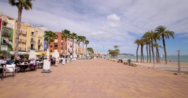 Villajoyosa, Valensiyalı İspanya, 12 Mart 2025: Villajoyosa kasabasındaki tipik bir İspanyol caddesinin, palmiye ağaçları ve restoranlarla dolu sahili gösteren görüntüsü