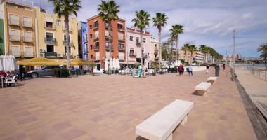 Villajoyosa, Valencia İspanya, 12 Mart 2025: Villajoyosa kasabasındaki tipik bir İspanyol caddesinin görüntüleri palmiye ağaçları, restoranlar ve altın kumlu plajları gösteriyor