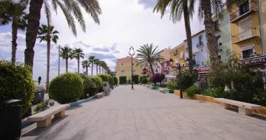 Villajoyosa, Valencia İspanya, 12 Mart 2025: İspanya 'nın Villajoyosa kentindeki tipik bir İspanyol caddesinin görüntüsü palmiye ağaçları ve restoranları ile caddeyi gösteriyor