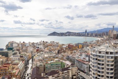 İspanya 'nın Benidorm kentinin havadan çekilmiş fotoğrafı, Platja de Ponent ya da Batı Sahili gezinti güvertesi olarak bilinen eski kentin arka planında dağlar ve bulutlar olduğunu gösteriyor.