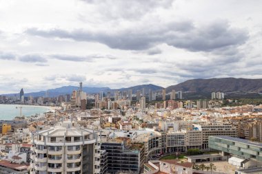 İspanya 'nın Benidorm kentinin havadan çekilmiş fotoğrafı, Platja de Ponent ya da Batı Sahili gezinti güvertesi olarak bilinen eski kentin arka planında dağlar ve bulutlar olduğunu gösteriyor.