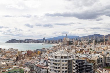 İspanya 'nın Benidorm kentinin havadan çekilmiş fotoğrafı, Platja de Ponent ya da Batı Sahili gezinti güvertesi olarak bilinen eski kentin arka planında dağlar ve bulutlar olduğunu gösteriyor.