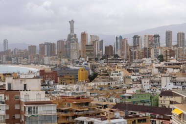 İspanya 'nın Benidorm kasabasındaki eski bir kasabaya bakan hava aracı fotoğrafı bulutlu bir günde, arka planda dağlar ve okyanuslar olan apartmanlar ve binalar gösteriyor.