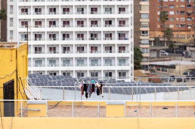 Temiz giysilerin kurutulduğu ve bir İspanyol apartman bloğunun tepesindeki çamaşır ipine tutturulduğu fotoğraf, binanın çatısında güneş panelleri olan yüksek katlı binanın üstündeki çamaşırların kuruduğunu gösteriyor.
