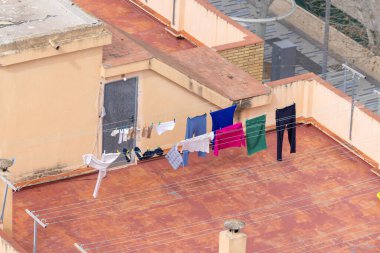 Temiz giysilerin kurutulduğu ve bir ispanyol apartmanının tepesindeki çamaşır ipine tutturulduğu fotoğraf. Çamaşırların yüksek binanın tepesinde kuruyup rüzgarın kıyafetleri üflediğini gösteriyor.