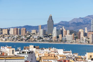 İspanya 'nın eski Benidorm kasabasına bakan hava aracı fotoğrafı güneşli bir günde Poniente sahilinde okyanus ve dağlarla çevrili binaları ve binaları gösteriyor.