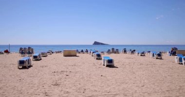 İspanya 'nın Benidorm kasabasının yavaş çekim görüntüleri, güneşli bir yaz gününde, okyanustaki adayla birlikte kumlu Levante Sahili' nde rahatlayan insanları gösteriyor.